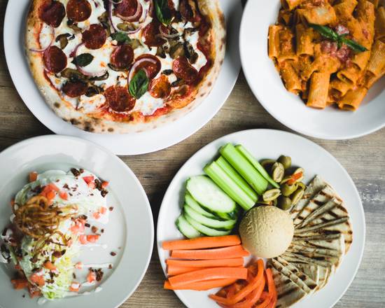Four plates of pizza, vegetables, and hummus on a wooden table.